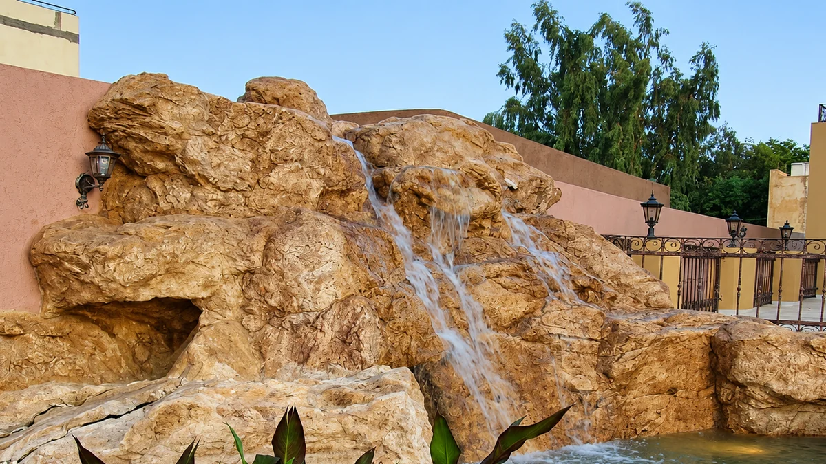 Sculpted rock waterfall spilling into a courtyard pool beneath wall lanterns